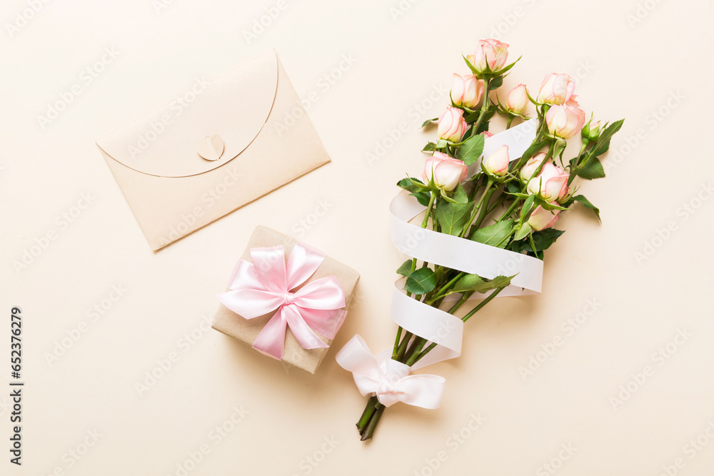 Fototapeta premium Greeting card mockup with copy space, pink ribbon and roses flowers on colored table background. Flat lay, top view. mother day holiday concept