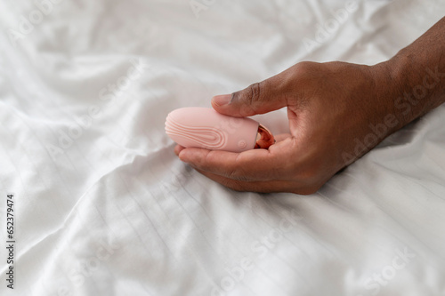 Hand of a young African man holding a pink vibrator, on a white sheet in a bed