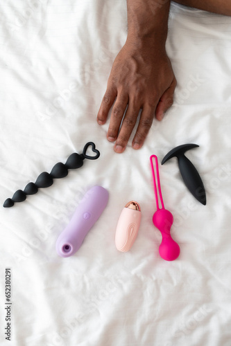Young African man s hand reaching for sex toy vibrators lying on the white bedding 