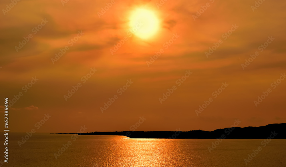 Beautiful sunset over the sea. Sun falling down behind the dark land. Red, orange and yellow color sky and clouds.