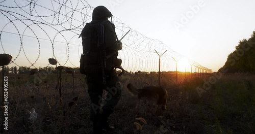 Soldier with service dog picking up trail, patrol state or private zone border at sunset. Security forces control boundary, protect from enemy and invasion photo