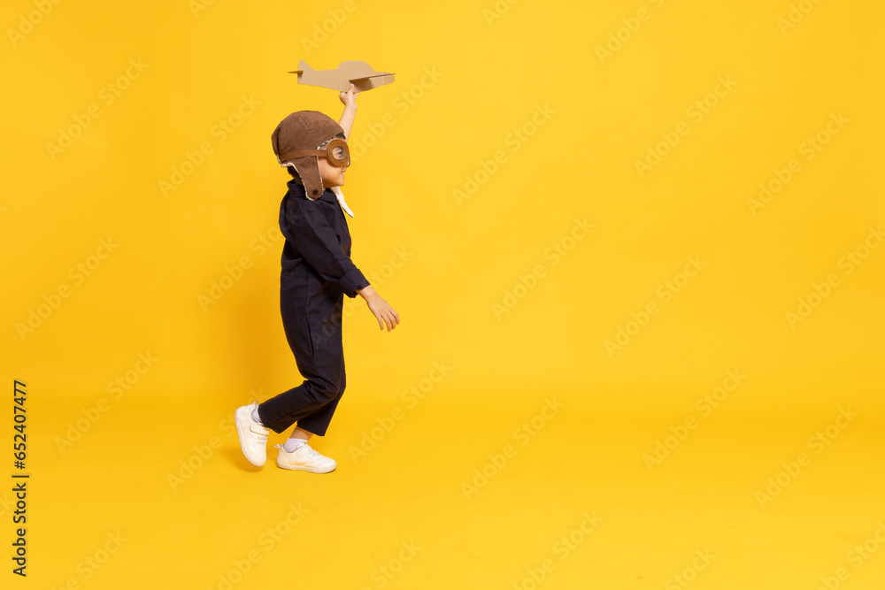 Side view of Asian little boy aviator running and playing with cardboard airplane isolated on yellow background - obrazy, fototapety, plakaty 