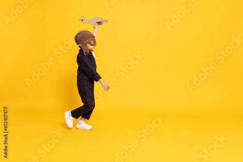 Side view of Asian little boy aviator running and playing with cardboard airplane isolated on yellow background