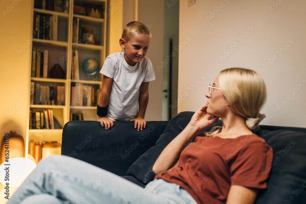 Obraz premium Young Caucasian boy coming to talk to his mother while she is having a phone call.