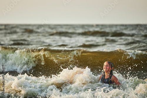 Little girl playing with waves in the sea. Kid playfully splashing with waves. Child jumping in sea waves. Summer vacation on the beach