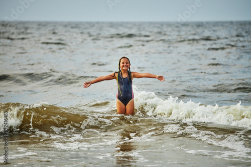 Little girl playing with waves in the sea. Kid playfully splashing in waves. Child jumping in sea. Vacations on the beach. Water splashes