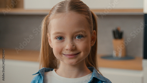 Moving camera close up portrait Caucasian cute little girl at home kitchen smiling looking camera domestic apartment headshot kid daughter posing indoors child schoolgirl smile happy adopted children