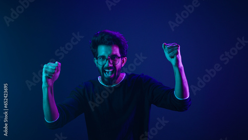 Happy Indian man in ultraviolet neon studio background champion coding achievement level up celebrating winning championship fan support victory supporter cheering competition excited goal spectator