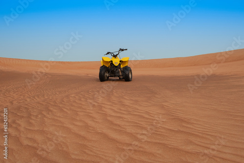ATV parked on a sand dune in the middle of the desert, sunny day, blue sky in the background. Extreme sports, adventure and travel concept.