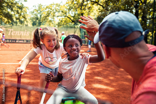 Young African American girl receiving positive feedback from her tennis coach on a outdoor clay court photo