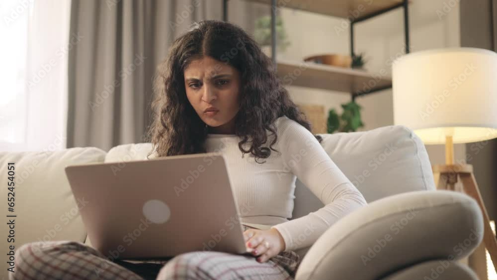Unhappy young curly woman feeling annoyed when getting message on laptop computer sitting on couch at home Nervous female having problem conflict online indoors. High quality 4k footage Unhappy young curly woman feeling annoyed when getting message on laptop computer sitting on couch at home Nervous female having problem conflict online indoors. High quality 4k footage