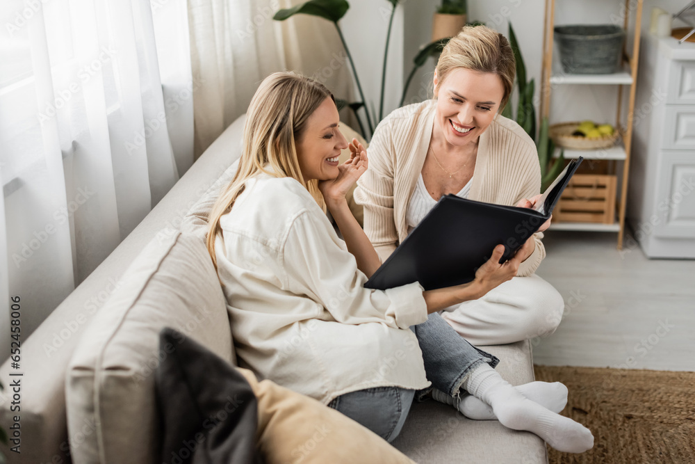 beautiful charming sisters smiling and looking at photo album, hand to chin, family bonding beautiful charming sisters smiling and looking at photo album, hand to chin, family bonding