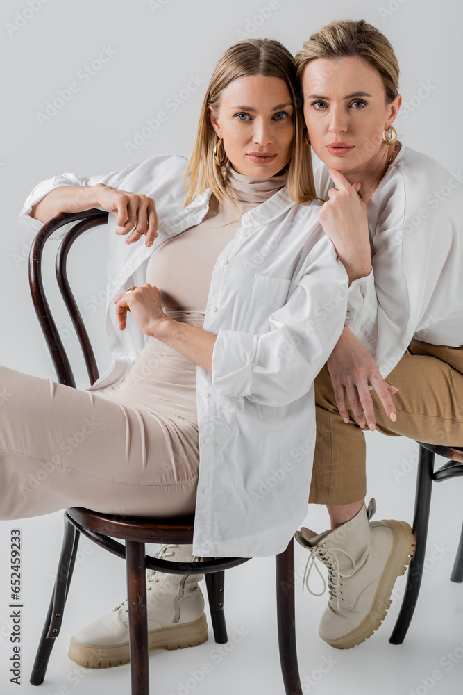 Obraz premium stylish elegant blonde sisters sitting on chairs in fashionable pastel attire, fashion concept