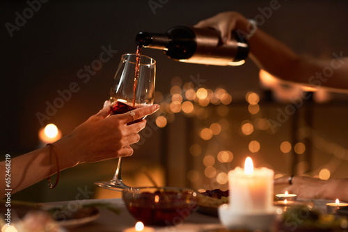 Side view closeup of two people pouring red wine into glass while enjoying dinner with candles  copy space