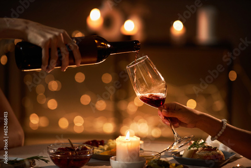 Side view closeup of two young women pouring red wine into glass while enjoying dinner with candles, copy space