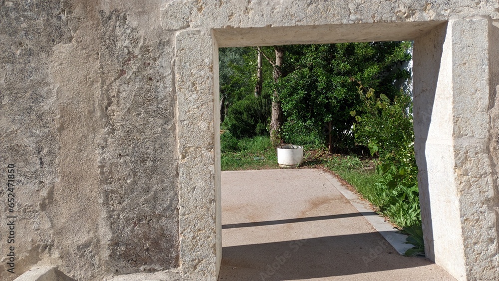 Obraz premium A window opening without it in the old wall, through which you can see the garden and courtyard