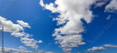 Small clouds in the blue sky. Low cumulus white clouds hang in the blue sky. They have different shapes and sizes. The clouds are white above and slightly gray below due to the lighting. © Andrew_Swarga