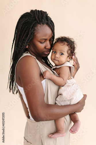 African-American mother with baby smiles and rejoices on beige background Minimalist portraits, space for text