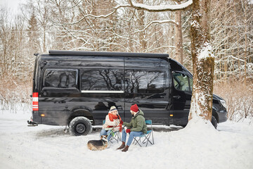 Wide angle portrait of young couple travelling by van outdoors in winter forest with cute dog, copy space