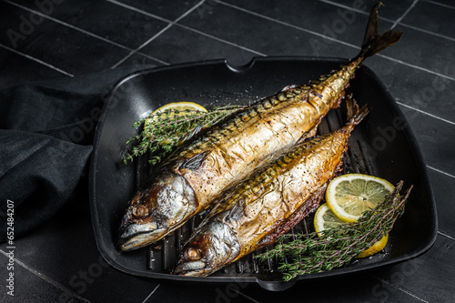 Grilled mackerel fish with lemon, herbs and spices in a skillet. Black background. Top view