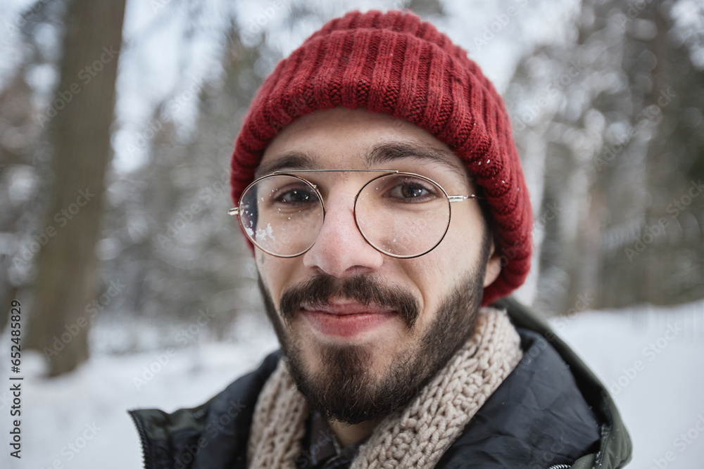 Close up portrait of bearded young man wearing glasses looking at camera outdoors in winter forest