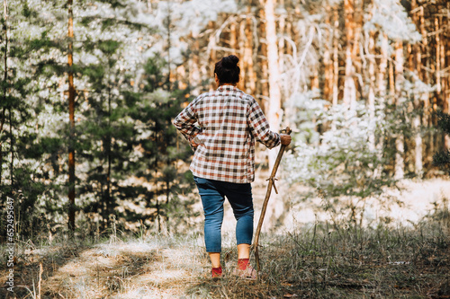 An adult elderly woman, a pensioner, a mushroom picker, walks with a stick through the forest in nature, doing tourism. Photography, healthy lifestyle concept.