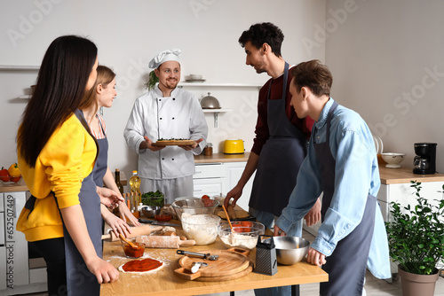 Italian chef with prepared pizza and group of young people after cooking class in kitchen