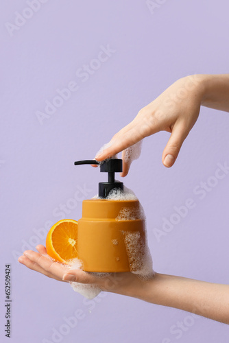 Hands with liquid soap and orange on lilac background