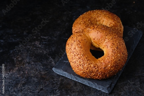 Two fresh bagels with sesame crust on a black slate board on a black concrete background.
