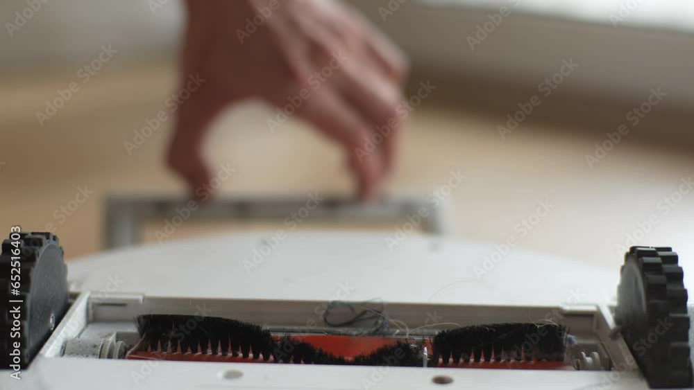 Close-up cropped shot of unrecognizable man taking out cleaning brush of robot vacuum cleaner to wash. Concept of wireless automatic cleaner maintenance and service. Shooting in slow motion. Close-up cropped shot of unrecognizable man taking out cleaning brush of robot vacuum cleaner to wash. Concept of wireless automatic cleaner maintenance and service. Shooting in slow motion.
