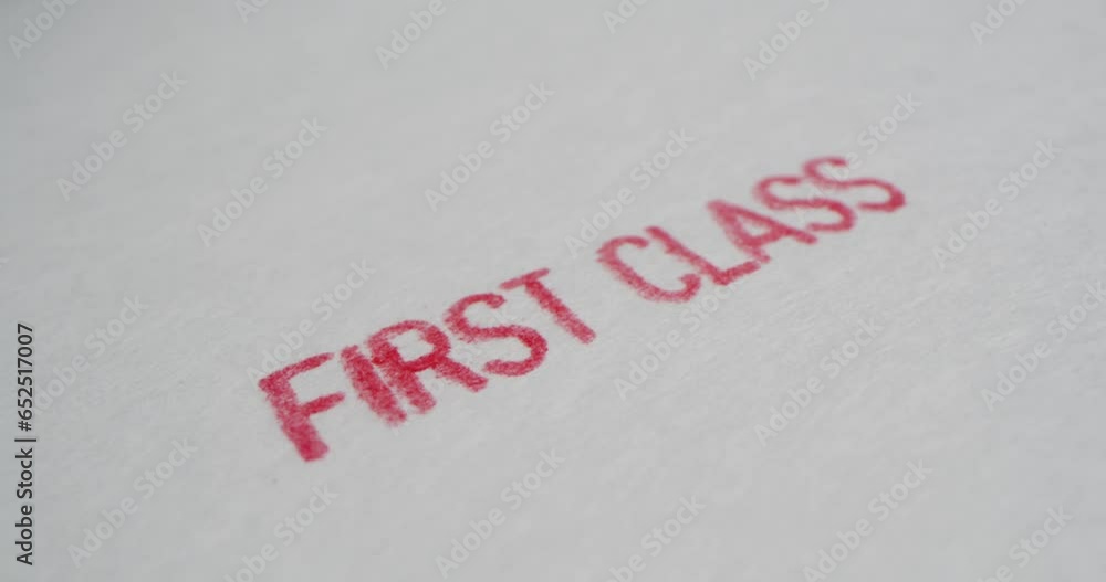 A stamp FIRST CLASS is placed on a sheet of white paper, close-up A stamp FIRST CLASS is placed on a sheet of white paper, close-up
