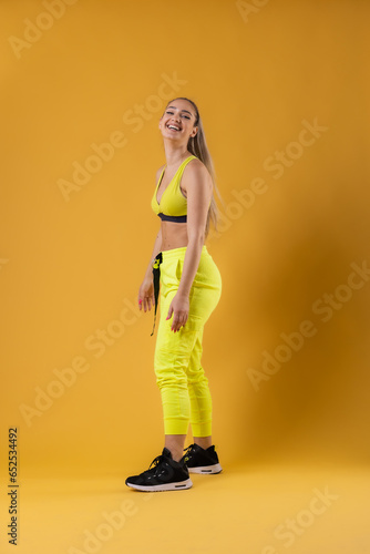 Beautiful happy girl in yellow outfit posing against dark yellow or orange background.