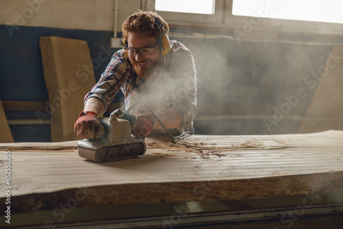 Professional male carpenter using electric sander for wood. Manufacture of wood products 