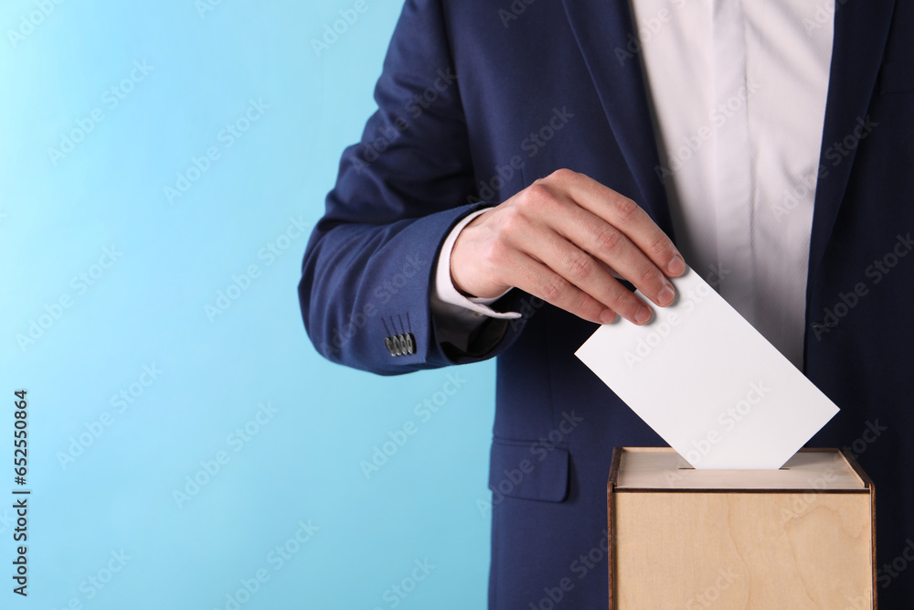 Man putting his vote into ballot box on light blue background, closeup. Space for text Man putting his vote into ballot box on light blue background, closeup. Space for text