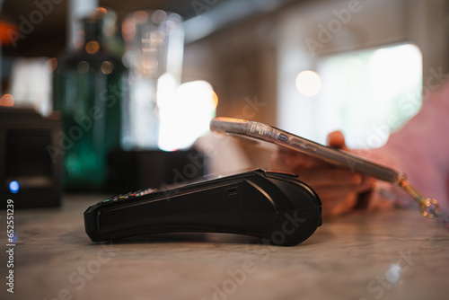 Close up view of young woman paying contactless with her smart phone on a POS at a restaurant