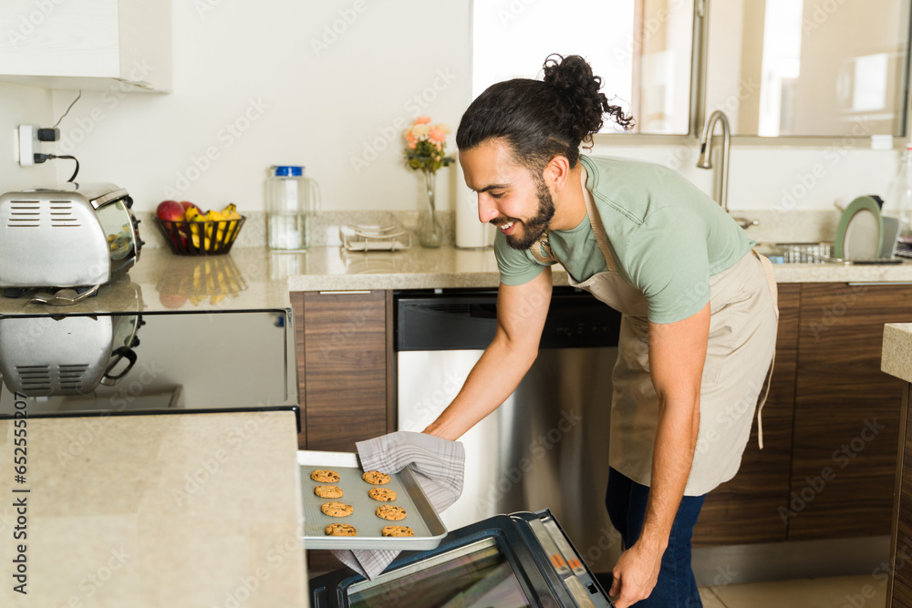 Happy man doing house chores baking cookies in the oven Happy man doing house chores baking cookies in the oven