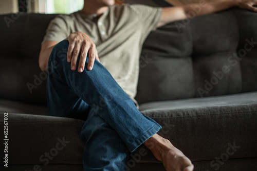 Young man sitting at home on couch with legs crossed relaxing enjoying day off 