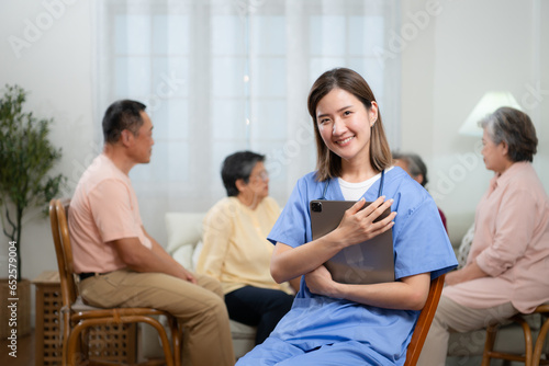 Portrait of Asian female nurse using digital tablet in nursing home with senior people on background