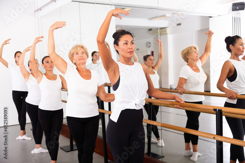 Concentrated asian woman rehearsing ballet dance in studio with other dancers