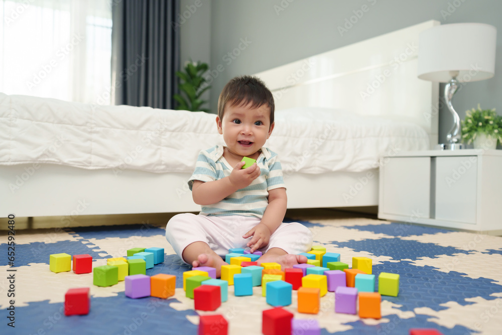 happy infant baby playing wooden block toy on jigsaw mat in bedroom happy infant baby playing wooden block toy on jigsaw mat in bedroom