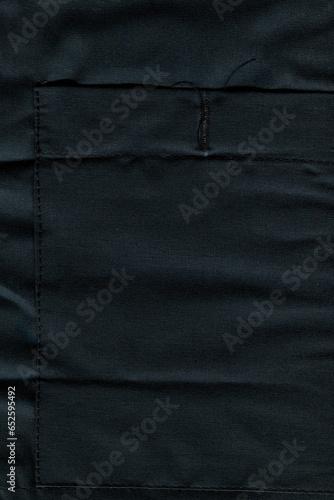 The texture of the coarse fabric is black. Coarse natural cotton fabric. Fabric for work clothes. Pocket on work clothes. Background of natural coarse fabric.