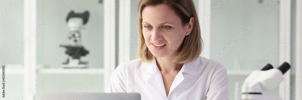 Satisfied female researcher working on laptop at laboratory table. Satisfied female researcher working on laptop at laboratory table.