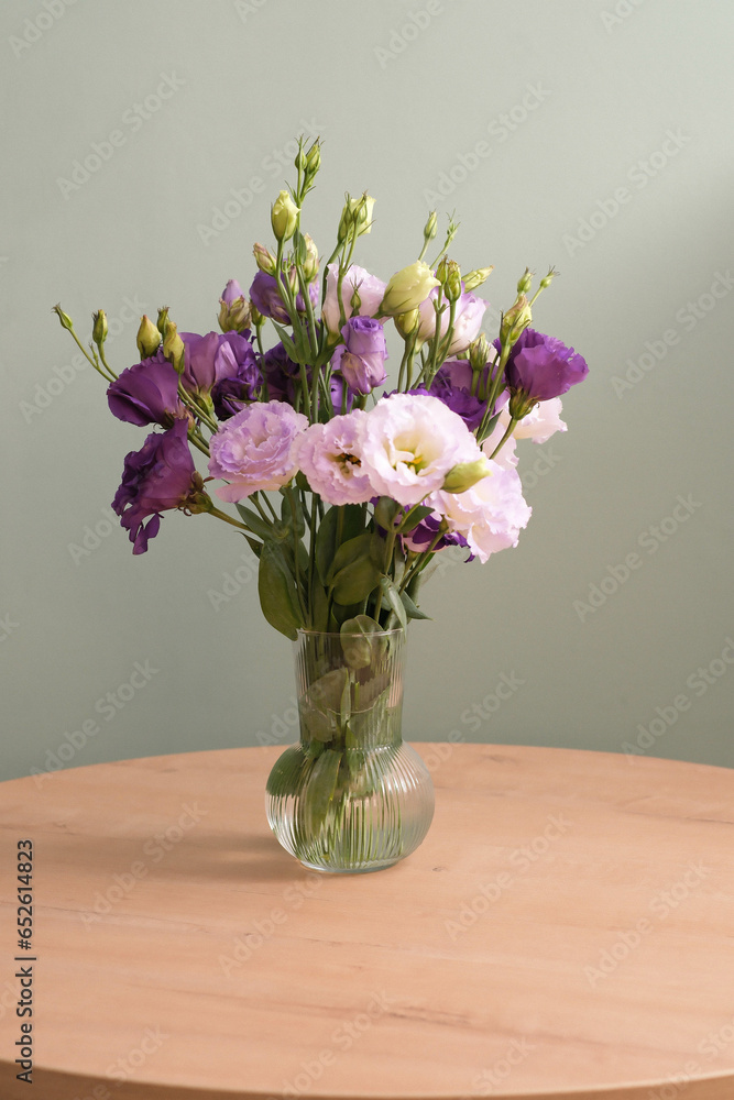 Obraz premium Bouquet of eustomas on a round wooden table on green background. Home interior.