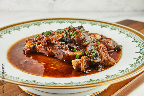 Ossobuco with garlic and green onions in red wine on plate with an ornament