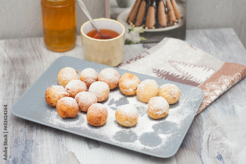 Curd donuts in powdered sugar on a plate, round donuts with a cup of tea Curd donuts in powdered sugar on a plate, round donuts with a cup of tea