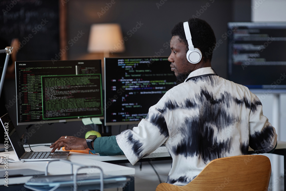 Young African American programmer in wireless headphones working with security codes at his workplace in IT office - obrazy, fototapety, plakaty 