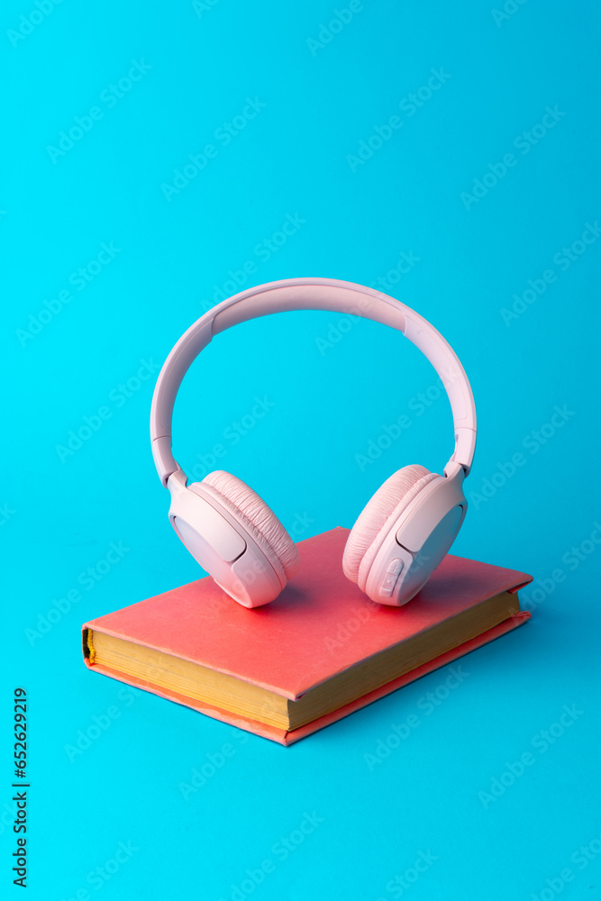 Pink headphones on a book on blue background Pink headphones on a book on blue background