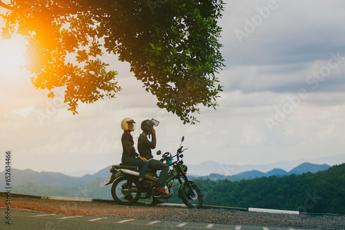 Fototapeta Naklejka Na Ścianę i Meble -  couples wearing safety helmet sitting on small enduro motorcycle against beautiful natural mountain scene at khaoyai national park thailand