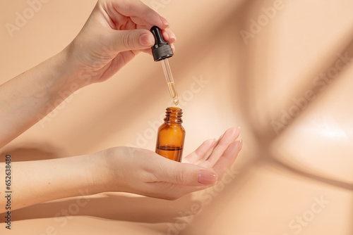 female hand with Dropper of essential oil, aromatherapy essence, beauty serum or medicinal liquid on beige background. Unbranded bottles for your design.