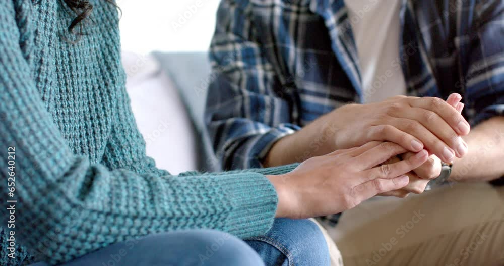 Midsection of biracial couple sitting on sofa and holding hands at home, in slow motion Midsection of biracial couple sitting on sofa and holding hands at home, in slow motion